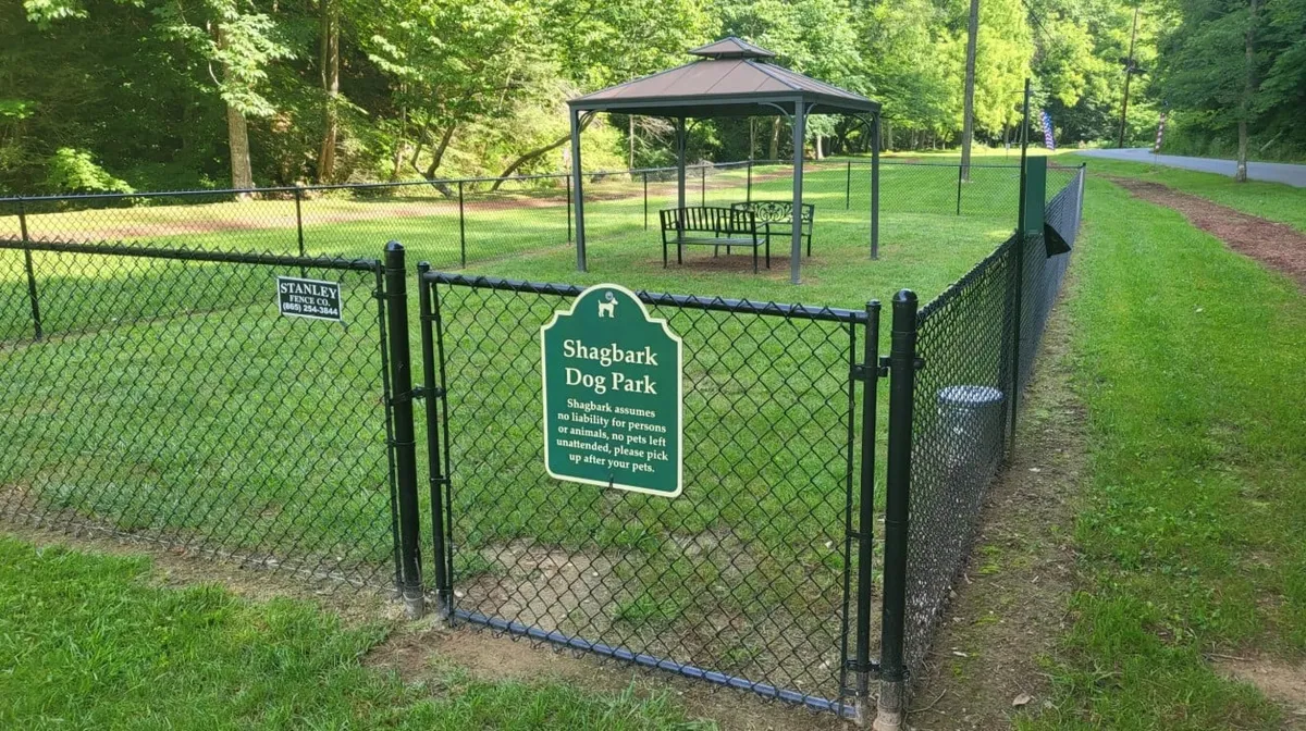 This image features a fenced area with a gazebo and signage, designed as a communal dog park space. The environment is inviting and well-maintained, providing a safe area for dogs to play and interact while owners relax or socialize under the gazebo.
