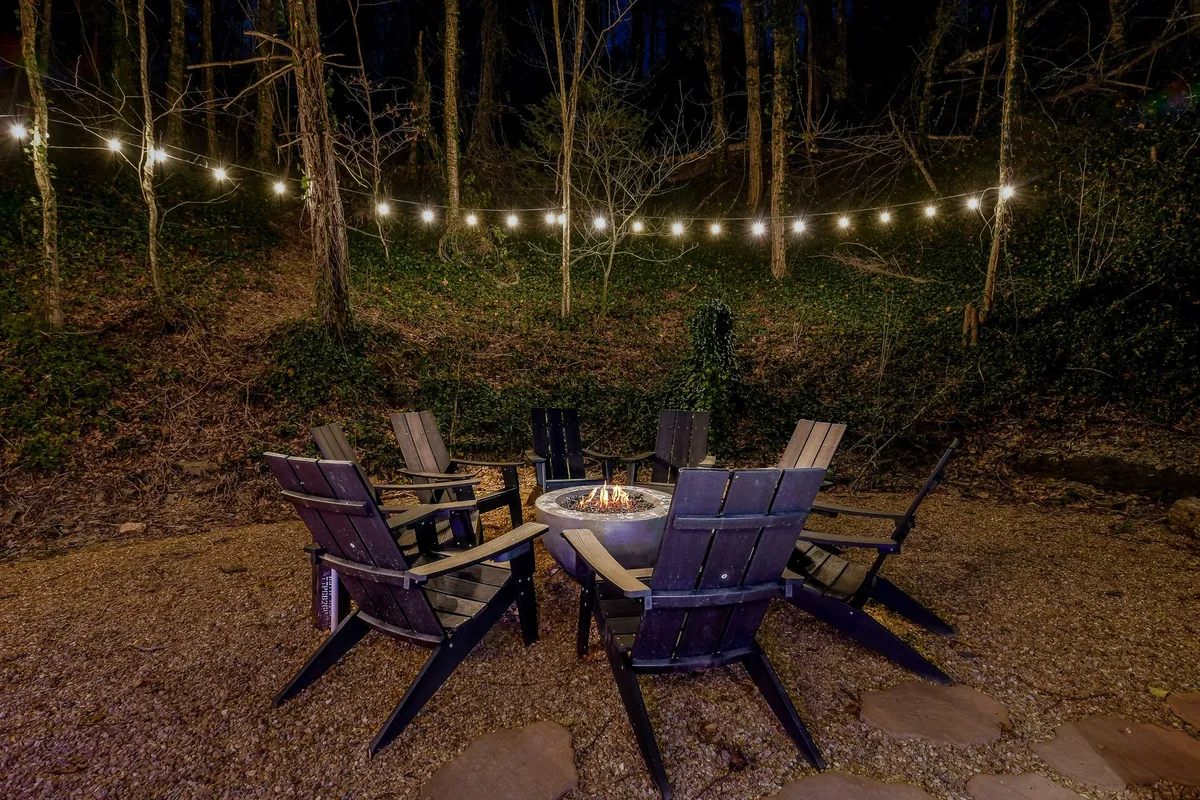 A warmly lit exterior scene showcasing a fire pit surrounded by Adirondack chairs and string lights. The inviting setup suggests a perfect spot for guests (and their pets) to relax after a day of adventure, sharing stories or unwinding under the stars.