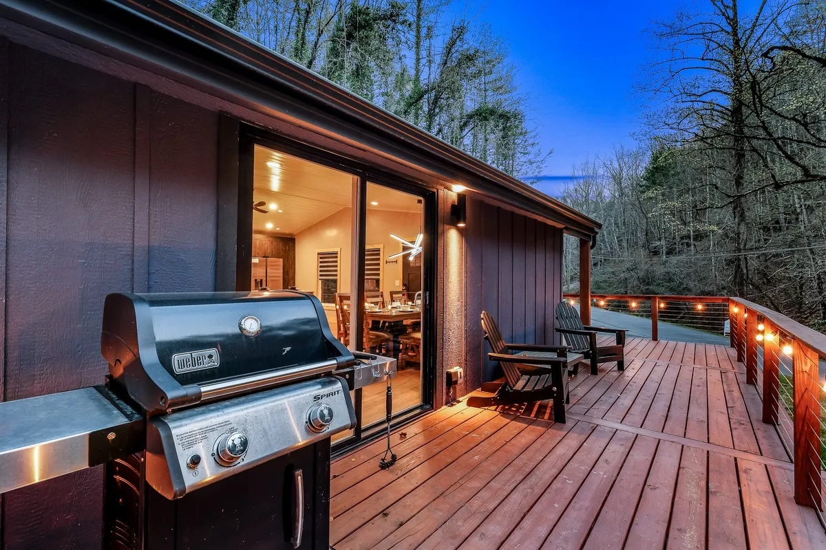 A spacious deck area with a modern grill, comfortable outdoor seating, and large windows looking into the cabin. The space is designed for outdoor dining and entertaining, blending seamlessly with the surrounding nature.
