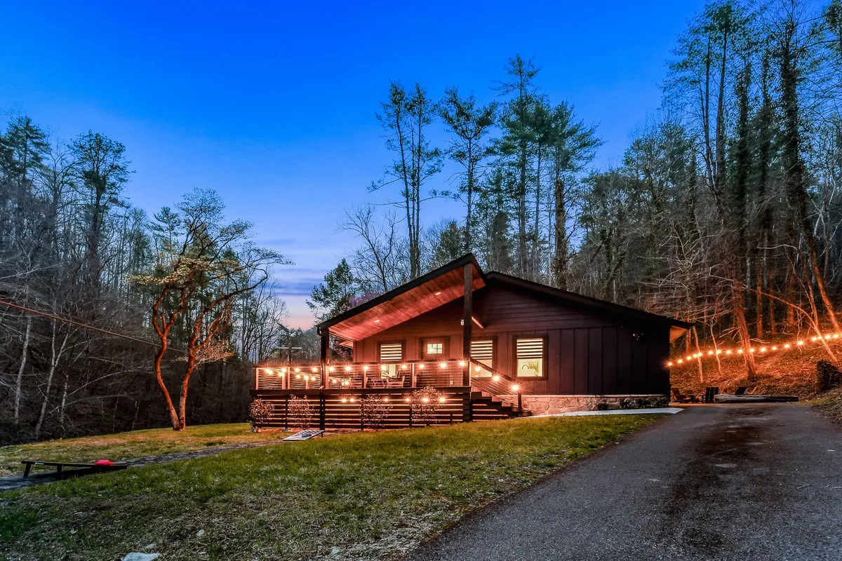 A wide shot of the house’s patio area adorned with string lights, surrounded by trees. The space is set up for outdoor dining and evening gatherings, capturing the inviting blend of comfort and natural surroundings. The deck offers a place to relax and enjoy mountain air.