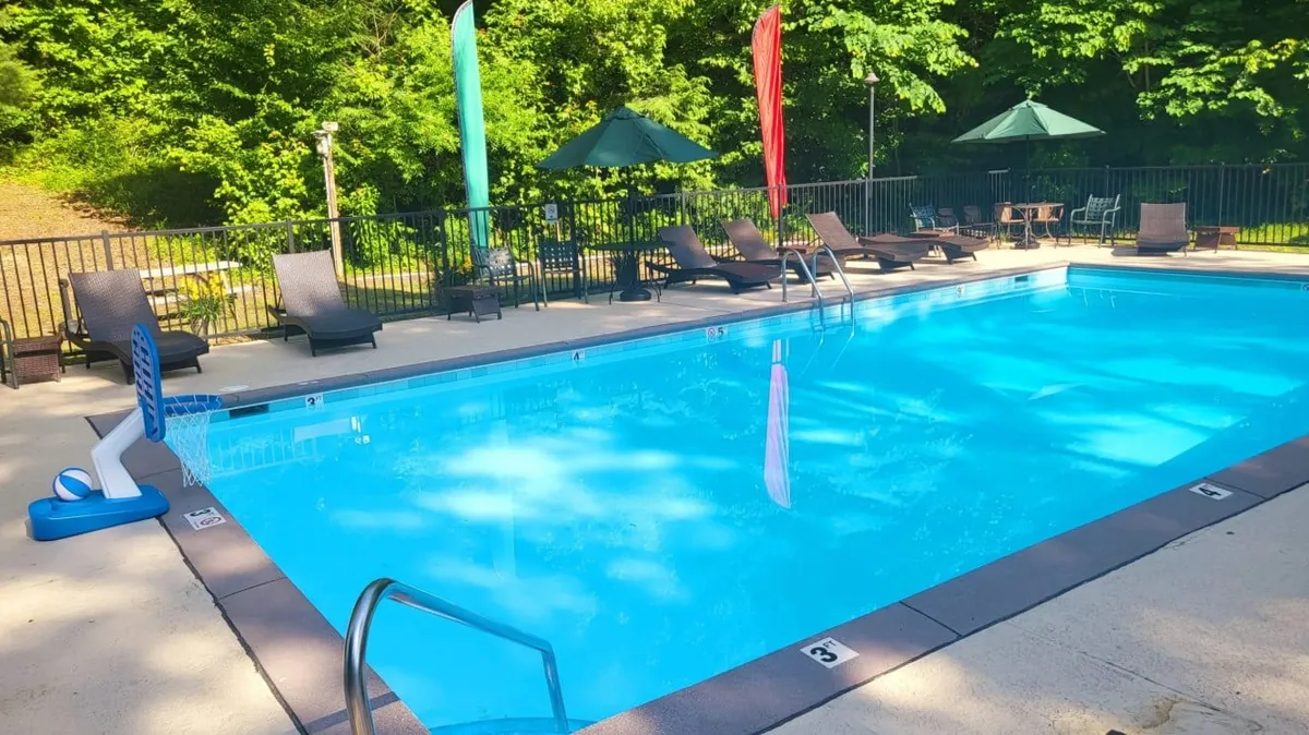This inviting scene showcases a sparkling swimming pool surrounded by lounge chairs, colorful flags, and shaded umbrellas. Families can be seen enjoying a refreshing swim and relaxing poolside, embodying the spirit of summer fun and relaxation.