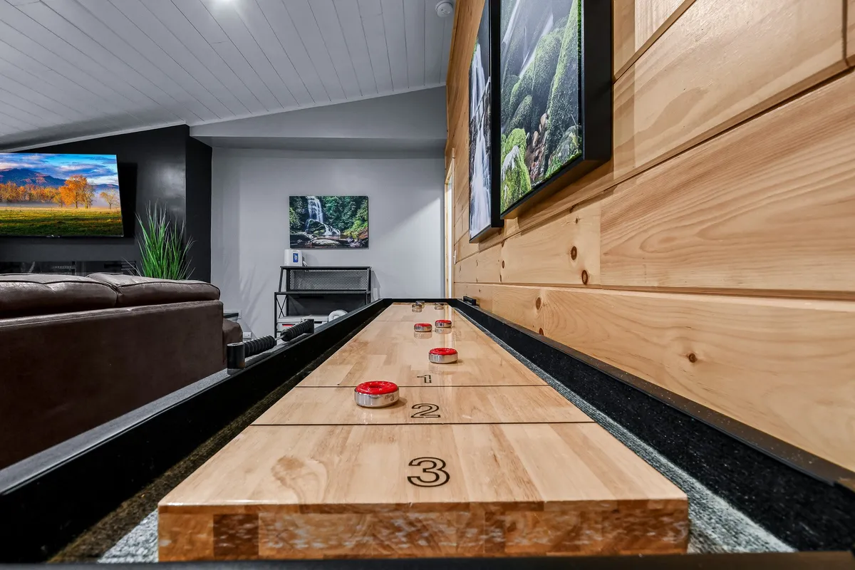A vibrant living space anchored by a shuffleboard table, a large television, and decorative wooden wall art. The room exudes a playful and relaxed vibe, perfect for friendly competition and entertainment.