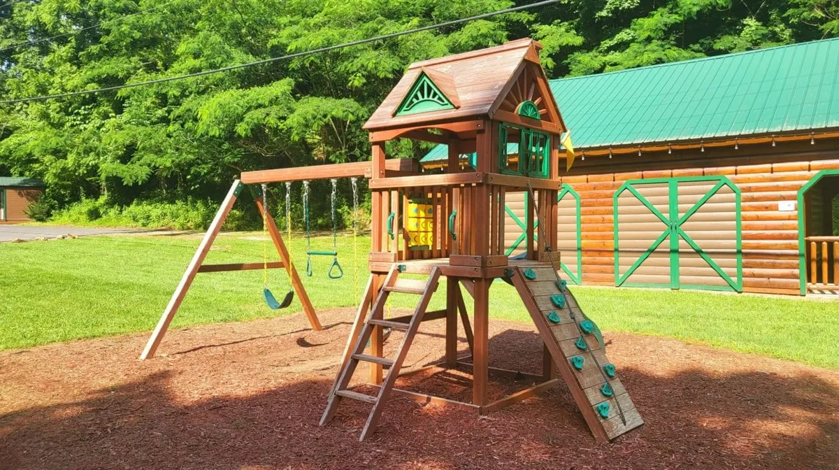This image features a vibrant playground structure complete with a swing set and climbing wall, surrounded by greenery. Children are seen playing and families gather around, capturing the joy and communal spirit of outdoor recreation.